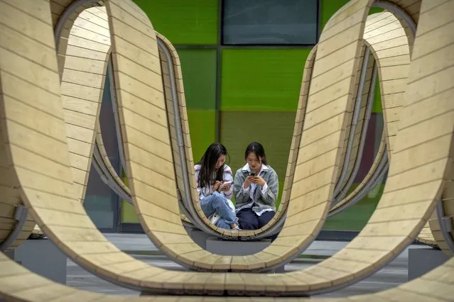 Women use their smartphones as they sit on a wooden structure at a shopping mall in Beijing, Saturday, May 6, 2023. (Photo by Mark Schiefelbein/AP Photo)