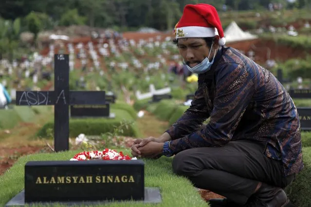 Indonesian Christian wearing protective face mask and Santa Claus hat make a pilgrimage to the grave of his family who died from Covid-19 coronavirus, during the 2020 Christmast day at the Covid-19 burial complex in the Pondok Rangon public cemetery, East Jakarta, on December 25, 2020. (Photo by Aditya Irawan/NurPhoto via Getty Images)