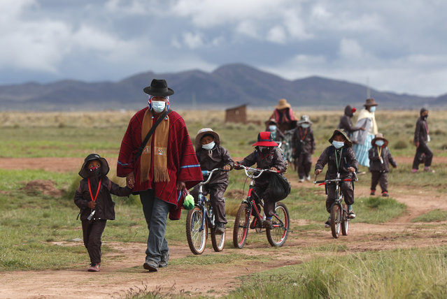 Aymaran Indigenous parents walk their children wearing new, protective uniforms to Jancohaqui Tana school as they return for their first week of in-person classes amid the COVID-19 pandemic, near Jesus de Machaca, Bolivia, Thursday, February 4, 2021. (Photo by Juan Karita/AP Photo)