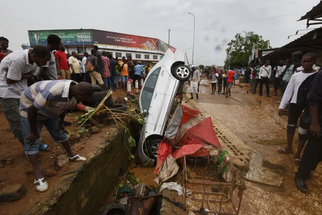 Pedestrians look at the wreckage of a vehicle lodged in a storm drain on a street in Abidjan on June 19, 2018, in which a man was reportedly found dead after floodwaters receded following an overnight downpour in the city. Fifteen people have died in Abidjan, Ivory Coast' s economic capital, during flooding caused by torrential rain overnight, Interior Minister Sidiki Diakite said. Rain poured down overnight on June 19, causing flash floods up to 2.5 metres (more than eight feet) deep, he said. (Photo by Sia Kambou/AFP Photo)