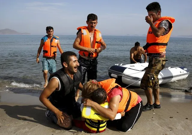 An Iranian migrant cries next to his son and wife moments after a small group of exhausted migrants from Iran arrive by paddling an engineless dinghy from the Turkish coast (seen in the background) at a beach on the Greek island of Kos August 15, 2015. (Photo by Yannis Behrakis/Reuters)