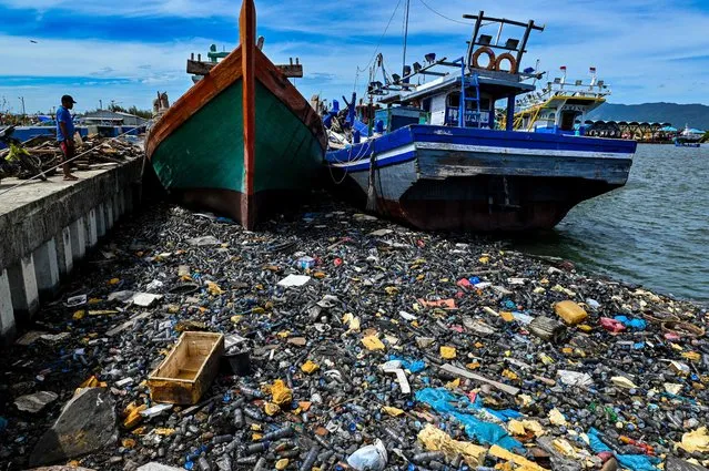 A man looks at garbage and plastic waste floating next to fishing boats at a port in Banda Aceh on June 5, 2023. (Photo by Chaideer Mahyuddin/AFP Photo)