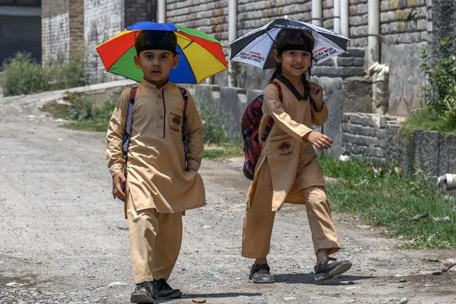 School children wearing umbrella hats to shelter from the sun, make their way to home along a street in Peshawar on June 19, 2023. (Photo by Abdul Majeed/AFP Photo)