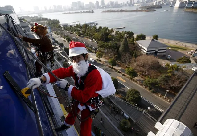 Window cleaners dressed as Santa Claus (R)  and a reindeer pose for photographers as he cleans a glass window at an event to celebrate the upcoming Christmas at a shopping mall in Tokyo December 24, 2015. (Photo by Issei Kato/Reuters)