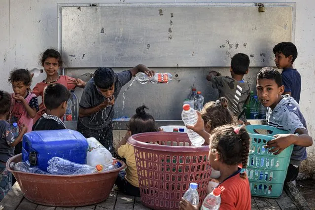 Palestinian children fill up water bottles from a cooler at a Bedouin village near Beit Lahia in the northern Gaza Strip on July 19, 2023 during a heat wave. (Photo by Mahmud Hams/AFP Photo)