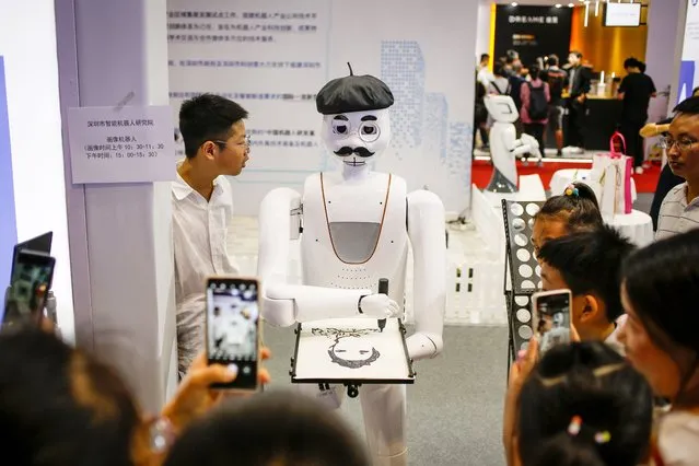 People watch as a robot draws a portrait during the World Robot Conference in Beijing, China, 18 August 2023. The yearly event is a platform for promoting exchanges and collaborations in the robotics sector. (Photo by Mark R. Cristino/EPA)
