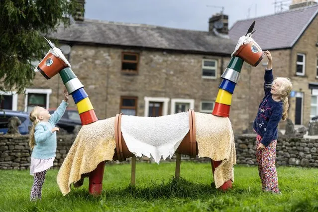 Holly, aged four, and her sister Scarlet, eight, play with a “pushmi-pullyu” llama made entirely of flowerpots at the annual flowerpot festival in the North Yorkshire market town of Settle in the second decade of August 2023. (Photo by Andrew McCaren/London News Pictures)