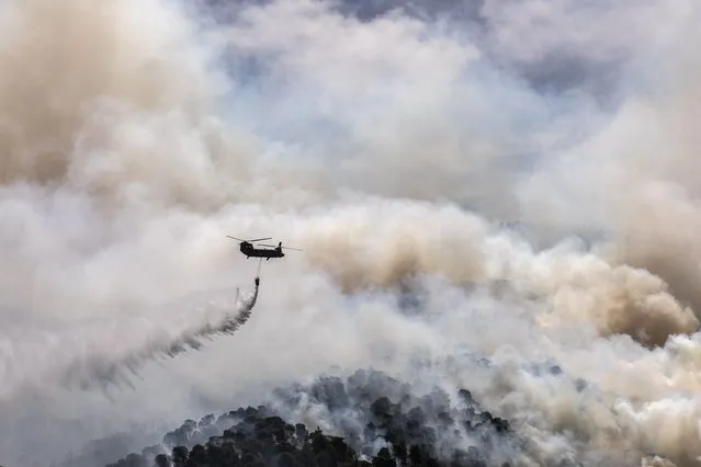 A military helicopter drops water over a forest near the village of Schinos, Corinth, Greece, on Thursday, May 20, 2021. (Photo by Petros Giannakouris/AP Photo)