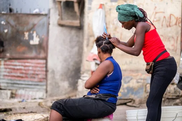 A woman combs another woman's hair in a Petion-Ville street market in Port-au-Prince, Haiti on July 18, 2021. (Photo by Ricardo Arduengo/Reuters)