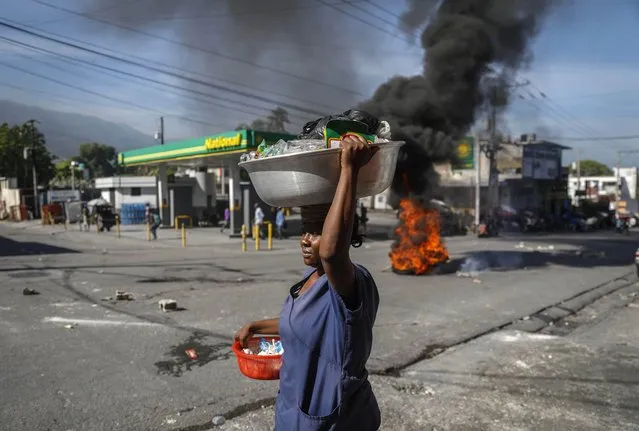 A food street vendor walks past tires set fire at a closed gas station as part of a protest against fuel shortages in Port-au-Prince, Haiti, Thursday, October 21, 2021. (Photo by Joseph Odelyn/AP Photo)