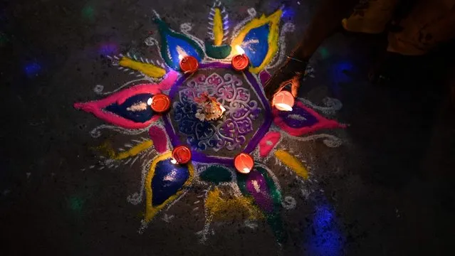 A woman places an oil lamp or “diya” on a rangoli during celebrations for the Hindu festival Diwali or the Festival of Lights in New Delhi on November 4, 2021. (Photo by Sajjad Hussain/AFP Photo)
