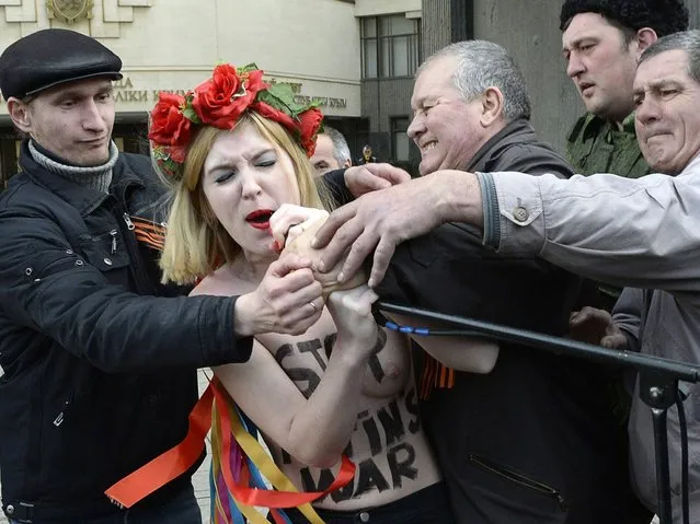 An activist of the Ukrainian women movement Femen tries to take the microphone away while protesting against the war in front of Cremea's parliament during a pro-Russian rally in Simferopol. (Photo by Alexander Nemenov/AFP Photo)