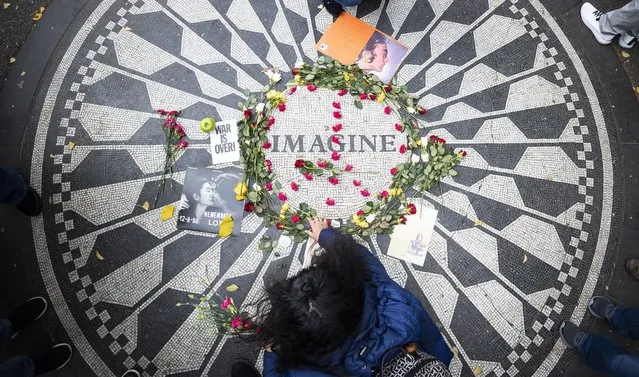 A woman lays flowers at the Strawberry Fields memorial to John Lennon in Central Park as musicians play Beatles songs for people gathered to mark the anniversary of Lennon’s death in New York, New York, USA, 08 December 2021. Today in 1980 John Lennon was shot and killed in front of his apartment building across the street from the park by Mark David Chapman. (Photo by Justin Lane/EPA/EFE)