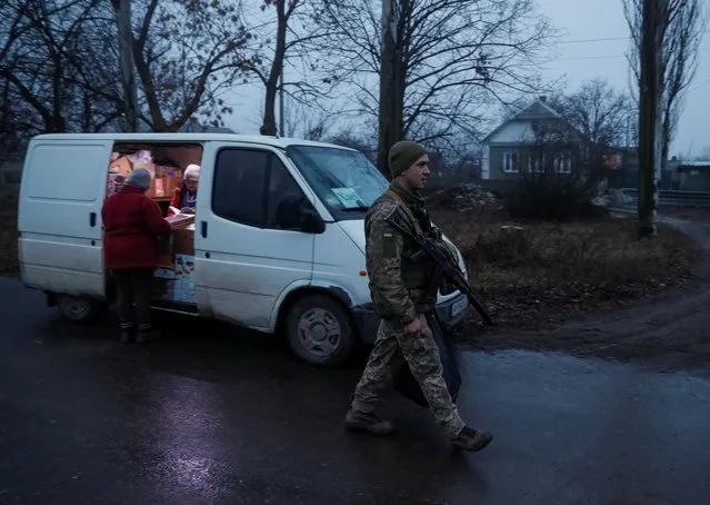 A local resident stands next to an auto shop as a Ukrainian service member walks along a street near the front line in the village of Travneve in Donetsk region, Ukraine, December 15, 2021. (Photo by Gleb Garanich/Reuters)