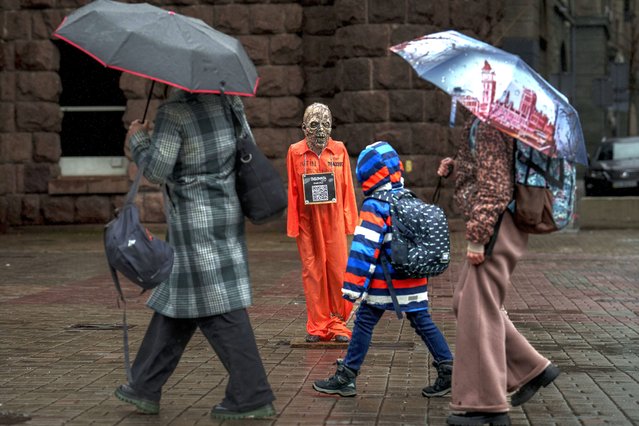 People walk by an effigy of Russian President Vladimir Putin dressed in a prisoner outfit during a rainfall in Kyiv, Ukraine, Monday, March 18, 2024. President Vladimir Putin secured a fifth term after the harshest clampdown on the opposition and free speech in the country since the Soviet era. (Photo by Vadim Ghirda/AP Photo)