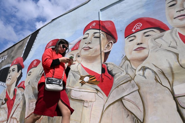 A woman uses her smartphone walking past a mural depicting members of Russia's Yunarmiya (Young Army) youth patriotic movement in Moscow on May 14, 2024. (Photo by Natalia Kolesnikova/AFP Photo)