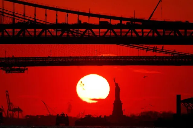 The sun sets behind the Statue of Liberty, Brooklyn Bridge, and Manhattan Bridge on January 31, 2022, in New York City. (Photo by Gary Hershorn/Getty Images)