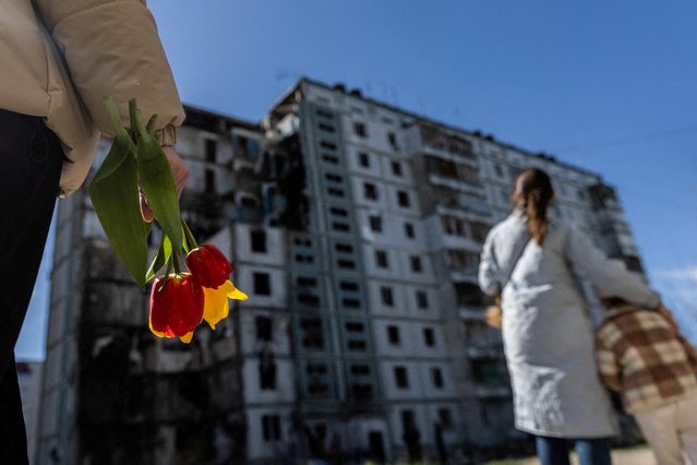 A woman carries flowers as she pays tribute to civilian people killed yesterday by a Russian missile strike, amid Russia's attack on Ukraine, at a strike site in the town of Uman, Cherkasy region, Ukraine on April 29, 2023. (Photo by Carlos Barria/Reuters)