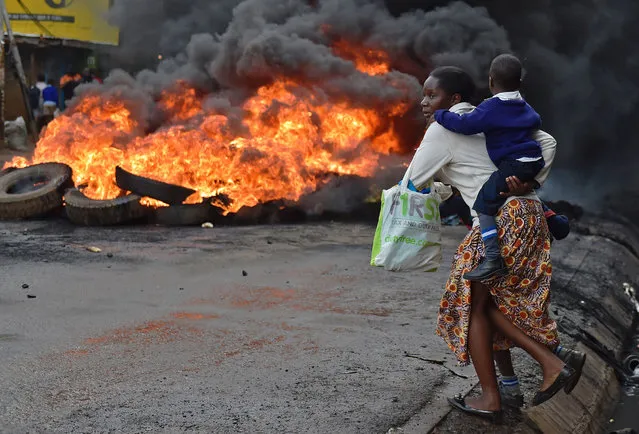 A woman carries a school pupil past a burning barricade in Kibera slum during a demonstration of opposition supporters protesting for a change of leadership ahead of a vote due next years, in Nairobi on May 23, 2016. (Photo by Carl De Souza/AFP Photo)