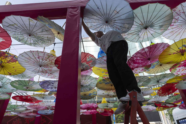 A worker sets up decoration formed with umbrellas for an outdoor market along the Wangfujing mall street in Beijing, Wednesday, June 19, 2024. (Photo by Ng Han Guan/AP Photo)