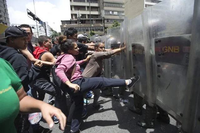 A woman kicks the shield of a National Guard soldier as others push them back them during a protest demanding food, a few blocks from Miraflores presidential palace in Caracas, Venezuela, Thursday, June 2, 2016. (Photo by Fernando Llano/AP Photo)
