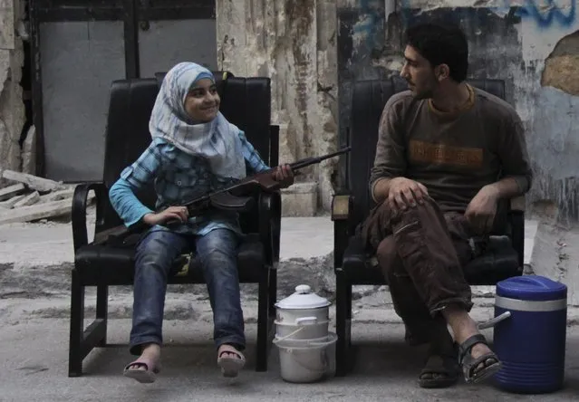 A girl holds a gun across her lap, as she sits with a Free Syrian Army fighter along a street in Aleppo on August 1, 2013. Picture taken August 1, 2013. (Photo by Loubna Mrie/Reuters)