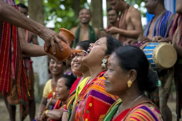 An Indian Rabha tribal Hindu priest serves traditional rice beer to the Rabha women in traditional attire as holy water during Baikho festival at Gamerimura village along the Assam Meghalaya border, west of Gauhati, India, Saturday, June 4, 2022. (Photo by Anupam Nath/AP Photo)