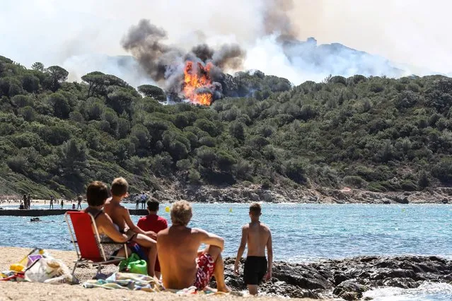 People enjoy the beach as they look at a forest fire in La Croix-Valmer, near Saint-Tropez, on July 25, 2017. Firefighters battle blazes that have consumed swathes of land in southeastern France for a second day, with one inferno out of control near the chic resort of Saint-Tropez, emergency services say. (Photo by Valery Hache/AFP Photo)