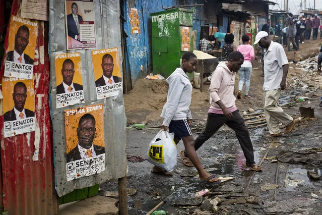 Kenyans walk past election posters in the Kibera slum in Nairobi, Kenya, Monday August 7, 2017. Kenyans are due to go to the polls on Aug. 8. to vote in presidential elections after a tightly-fought race between President Uhuru Kenyatta and main opposition leader Raila Odinga. (Photo by Jerome Delay/AP Photo)