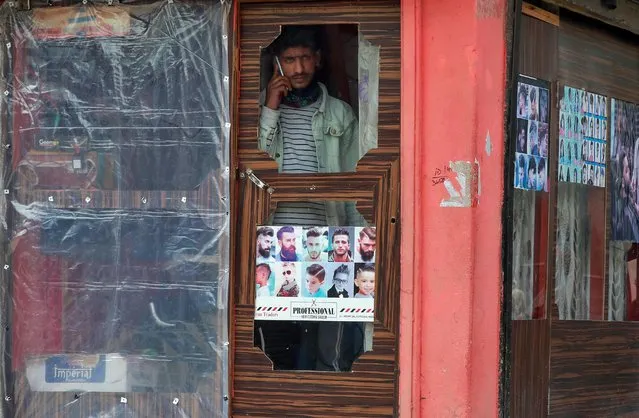 A man speaks on his mobile phone as he looks out from a barber shop in Srinagar on February 6, 2020. (Photo by Danish Ismail/Reuters)