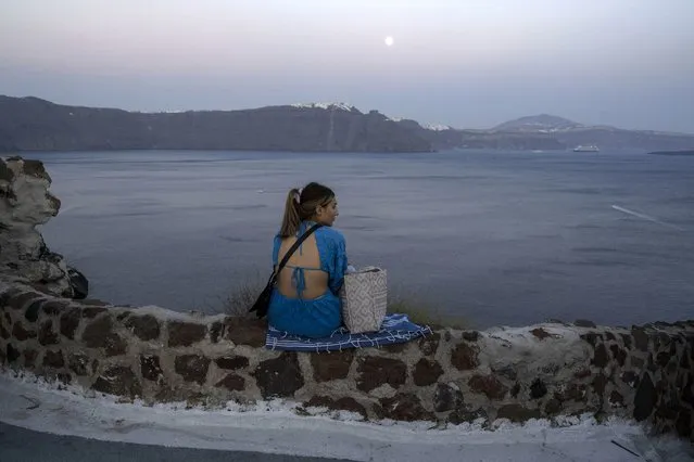 A woman looks on the Aegean Sea as the moon rises in Santorini island, Greece, on Monday, June 13, 2022. (Photo by Petros Giannakouris/AP Photo)