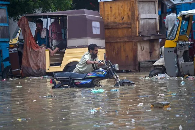 A man pushes his motorbike through a flooded street after heavy monsoon rainfall in Karachi on July 25, 2022. (Photo by Rizwan Tabassum/AFP Photo)