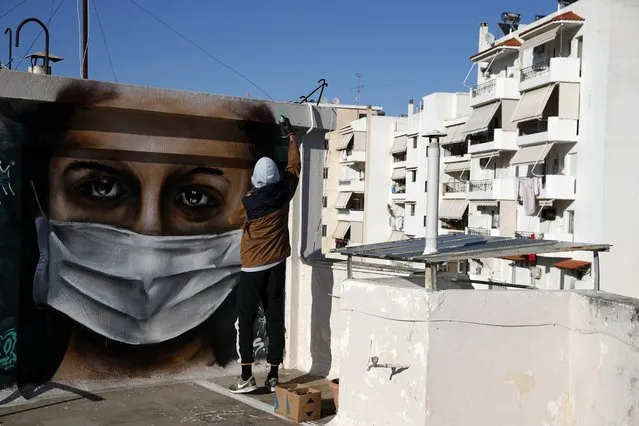 S.F., a 16-year-old Greek graffiti artist, spray-paints a design, a woman wearing a face mask referring to protection against coronavirus, on the roof of his apartment block in Athens, Tuesday, March 17, 2020. Greece has imposed a wide range of public safety measures to try and contain the coronavirus outbreak, including school and store closures. The vast majority of people recover from the new coronavirus. According to the World Health Organization, most people recover in about two to six weeks, depending on the severity of the illness. (Photo by Thanassis Stavrakis/AP Photo)