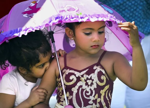 Five-year old Vyahi Bidrahalli, right, a student with the Peoria Ballet along with sister Gaya Bidrahalli, 3, try to keep cool in the shadow of an umbrella with temperatures reaching into the 90's while waiting to perform on the stage at a Kid's Day in East Peoria, Ill., Saturday, July 23, 2016. (Photo by Ron Johnson/Journal Star via AP Photo)