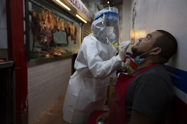 A medical worker from the Ministry of Health wearing a protective suit takes a sample to test for COVID-19 from a butcher at La Terminal market in Guatemala City, Thursday, May 21, 2020. (Photo by Moises Castillo/AP Photo)