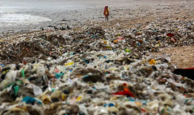 A life guard walks past a plastic waste and garbage washed ashore during monsoon at seashore of Juhu beach in Mumbai, India, 08 July 2022. The city’s coastline witnesses serious garbage crisis as people dump their trash directly into nullahs or storm water drains, rivers and creeks, brought back on the beaches during the monsoon season. The Brihanmumbai Municipal Corporation (BMC) has prohibited general public from visiting the beaches as the Meteorological Department issued a red alert in Mumbai. (Photo by Divyakant Solanki/EPA/EFE)