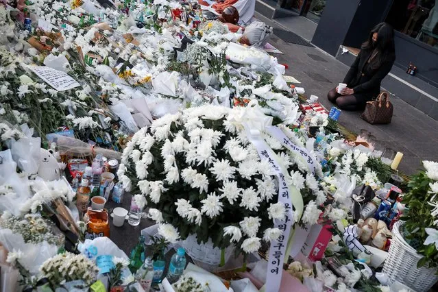 A woman kneels next to floral tributes near the site of a crowd crush that happened during Halloween festivities, in Seoul, South Korea on November 2, 2022. (Photo by Kim Hong-Ji/Reuters)