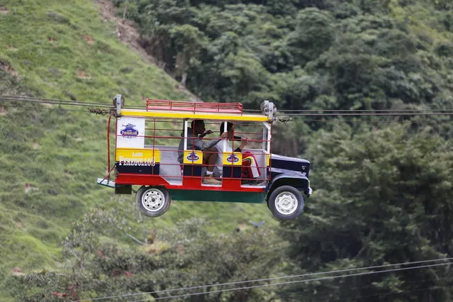 Tourists ride a cable car in the form a of a Chiva, a bus used to serve rural routes, in Pitalito, Colombia, Tuesday, April 5, 2017. The ride called “La Chiva Voladora” costs about $0.70 and you zip along about 800 meters from one side of a hill to another. (Photo by Fernando Vergara/AP Photo)