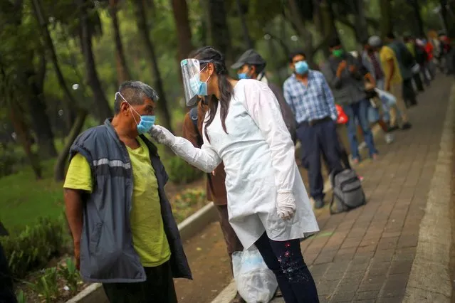 A medical staff scans the temperature of a man lining up for free food at a public park, as the outbreak of the coronavirus disease (COVID-19) continues in Mexico City, Mexico, July 30, 2020. (Photo by Edgard Garrido/Reuters)