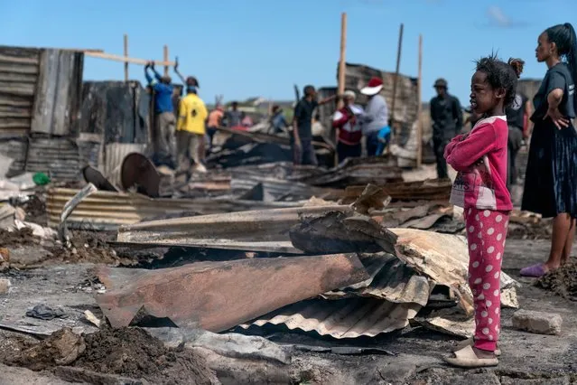A girl looks on as residents begin to rebuild shacks after a fire raged through Z section of Masiphumelele informal shack settlement, Cape Town, South Africa, 22 November 2022. An initial estimate by nonprofit group Gift of the Givers on scene indicates more than 800 shacks were destroyed and more than 1,500 people displaced in the fire which raged 21 November. Nonprofit groups Gift of the Givers and Living Hope are providing humanitarian aid in the densely populated Masiphumelele shack district. Masiphumelele is particularly susceptible to fire with poor access routes hampering firefighting efforts. This was the second big fire in a month in the area. (Photo by Nic Bothma/EPA/EFE/Rex Features/Shutterstock)