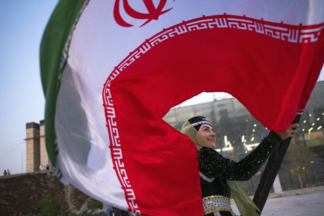 A young woman wearing a traditional style headscarf and dress waves an Iranian flag after performing in a flag ceremony, marking Iran's Islamic Republic National Day, in the Abbasabad Cultural and Tourist Area in central Tehran, Iran, on April 1, 2025. (Photo by Morteza Nikoubazl/NurPhoto/Rex Features/Shutterstock)