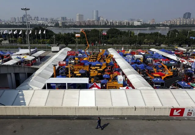 A man walks past construction vehicles on display during the China Import and Export Fair, also known as Canton Fair, in the southern Chinese city of Guangzhou October 15, 2015. (Photo by Bobby Yip/Reuters)