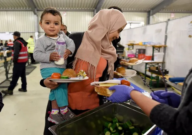 A migrant holding her child receives food in a refugee camp in Celle, Lower-Saxony, Germany October 15, 2015. With the approach of winter, authorities are scrambling to find warm places to stay for the thousands of refugees streaming into Germany every day. In desperation, they have turned to sports halls, youth hostels and empty office buildings. (Photo by Fabian Bimmer/Reuters)