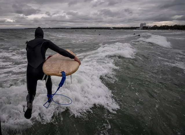 A surfer jumps into the Baltic Sea in Timmendorfer Strand, northern Germany, Wednesday, October 14, 2020. Strong winds and unusual high waves changed the normally quiet sea into a surfer hot spot. (Photo by Michael Probst/AP Photo)