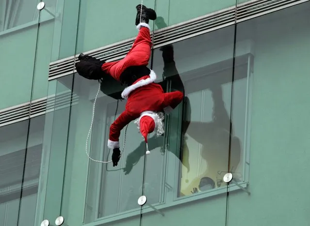 A member of the police special forces dressed in a Santa Claus suit waves to a patient as he abseils from the roof of a paediatric clinic in Ljubljana December 16, 2014. (Photo by Srdjan Zivulovic/Reuters)