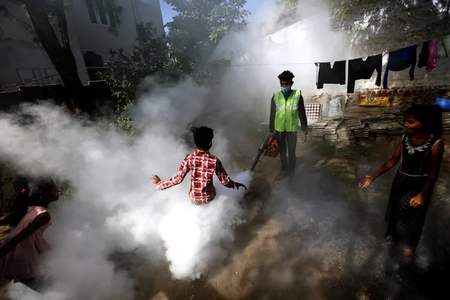 A boy plays smoke from fumigation being carried out by a municipal worker at a residential area in Ahmedabad, India, Thursday, December 3, 2020. (Photo by Ajit Solanki/AP Photo)