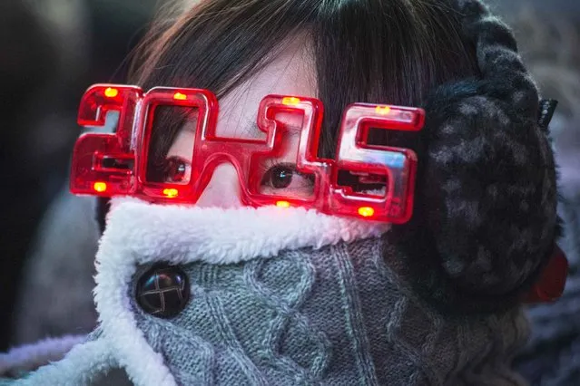 A woman wears 2015 glasses while taking cover from the cold weather during New Year's Eve celebrations in Times Square, New York December 31, 2014. (Photo by Stephanie Keith/Reuters)