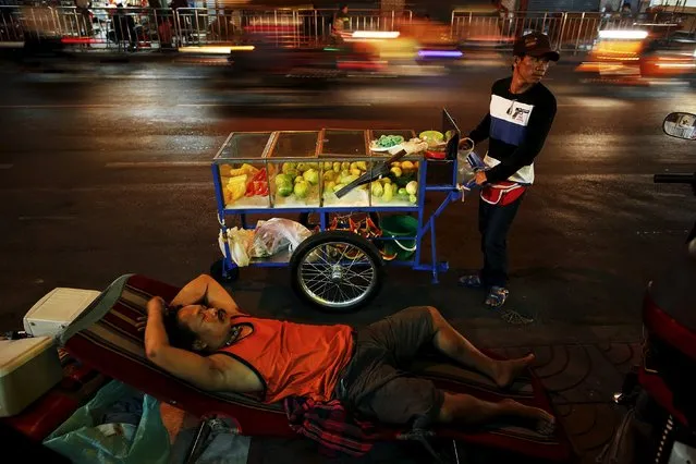 A street vendor pulls his cart by a sleeping man as cars pass by in Bangkok's Chinatown in this February 6, 2013 file photo. (Photo by Damir Sagolj/Reuters)