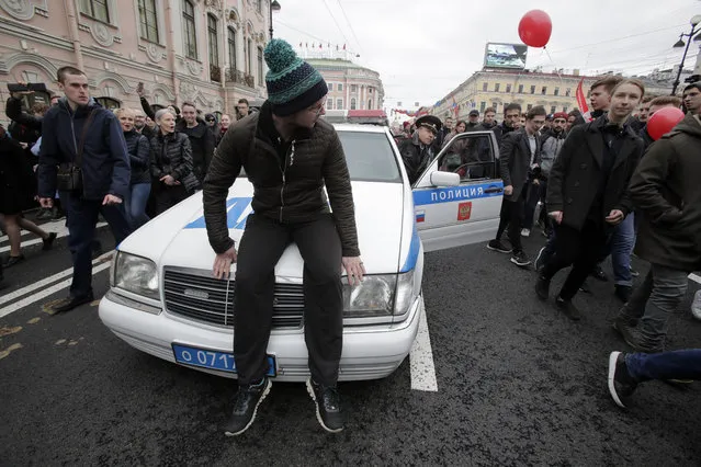A demonstrator sits on a police car to stop it during a protest rally in St.Petersburg, Russia, Saturday, May 5, 2018. Alexei Navalny, anti-corruption campaigner and Putin's most prominent critic, called for nationwide protests on Saturday, two days ahead of the inauguration of Vladimir Putin for a fourth term as Russian president. (Photo by Dmitri Lovetsky/AP Photo)