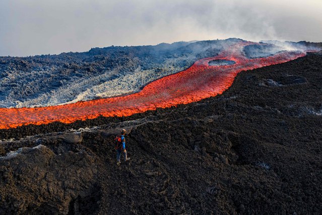 This aerial view shows a man standing near a flow of lava on the Mount Etna volcano (Torre del Filosofo - Etna Sud) on August 28, 2025. The Etna volcanic eruption started on August 10 and remain active the last weeks. (Photo by Giuseppe Distefano/AFP Photo)